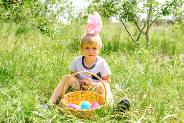 Easter egg hunt.Little boy child kid in bunny ears picking up eggs in grass,garden.Easter holiday...