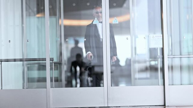 施設の自動ドアから屋外に出てくるタキシードを着た紳士