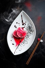 Tuna slices with soy sauce and sesame seeds on a polished dark surface with chopsticks