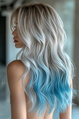 Naklejka premium Close-up portrait of a woman with long, wavy silver hair transitioning into vibrant blue ombre, styled in soft curls, indoors.