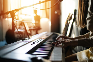 Woman playing digital piano in sunlit music studio surrounded by guitars and recording gear, concept of creativity, music production, lifestyle and female artists. © DedMityay