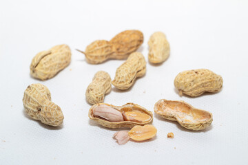 Several peanuts in their shells, scattered on a white surface, with one shell broken open revealing the nuts inside.