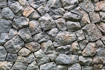 Stone wall texture. Close-up of a wall made of irregularly shaped, gray and brown stones. Rough and...