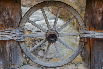 The wooden wheel between wooden pole and a 
 stream in the background in Carpathian Mountains in Autumn.