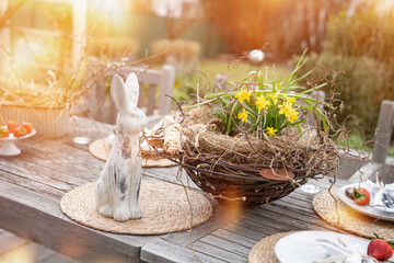 Fresh table set in garden with easter decoration. Easter bunny with spring flowers on wooden table...