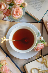 A cup of aromatic tea, a book and a rose on the table.