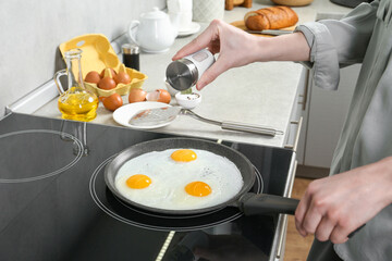 Woman adding salt into frying pan while cooking eggs on cooktop in kitchen, closeup