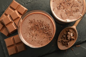 Tasty chocolate milk with shavings and pieces on black table, flat lay