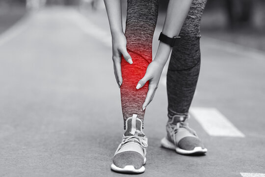 Shin Splints Injury. Female Athlete Massaging Injured Leg, Suffering From Trauma During Jogging In Park, Black And White Image With Red Sore Spot