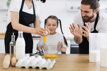 Caucasian family showing father, mother, and young daughter cooking meal in kitchen setting. Family...
