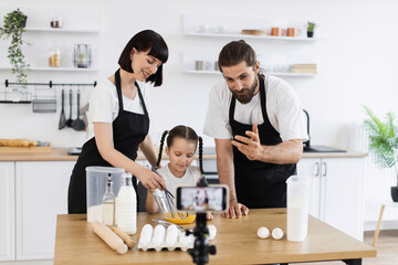 Caucasian family of bloggers filming cooking tutorial in kitchen. Parents teaching daughter baking....