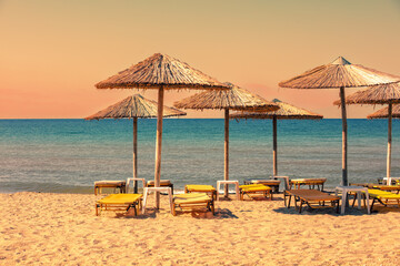 Tropical beach scenery with sun parasols and evening sky. Straw sun umbrellas on the beach