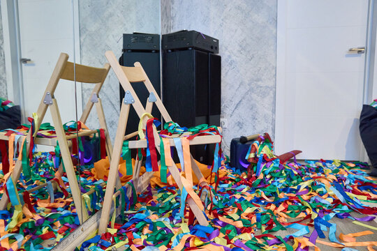 Empty wooden chairs surrounded by a vibrant array of colorful confetti ribbons after a festive celebration. The scene captures the aftermath of a lively, joyful party event.