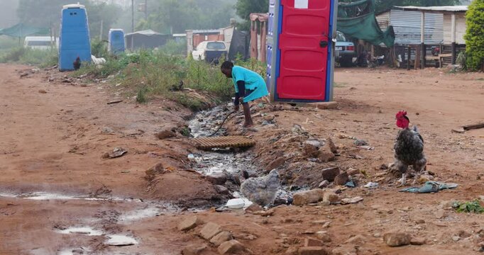 Poverty. Inequality. A young Black African boy plays in stinking dirty effluent water next to portable toilets in a township in Africa