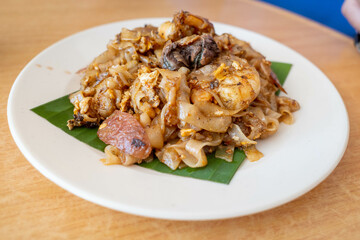 A plate of char koay teow or stir fried flat rice noodle dish made popular in Penang Malaysia. It is smoky flavor, sweet and savory with prawns, cockles and sausages.