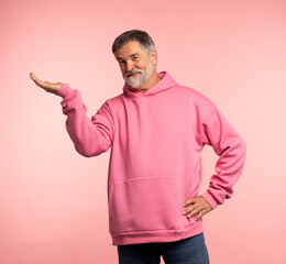 Happy middle aged man in pink sweatshirt presenting ads advertising product or service isolated on pink background