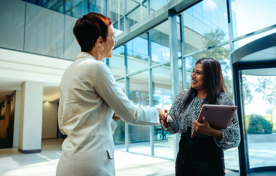 Professional businesswomen shaking hands in a bright modern office lobby - Powered by Adobe