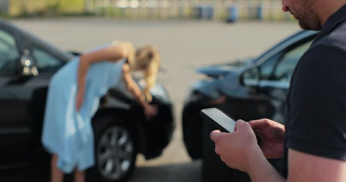 Man insurance agent inspects damage to a woman car and makes notes on a smartphone. Man inspecting broken car. Insurance concept.
