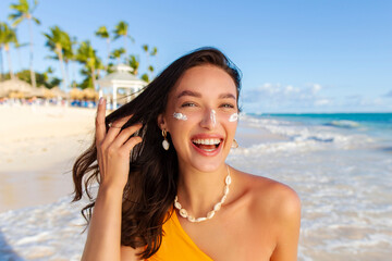 Portrait of happy woman posing with sun cream protection lotion on face, standing on beach with...