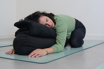 Obraz premium young woman on a mat reclining on pillows to relax her neck and spine.