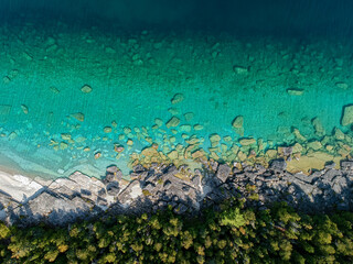 Aerial 90 degree straight down photo of emerald crystal clear water, rocky shore overgrown with...