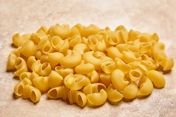 Wide-angle view of a pile of dry yellow pipe rigate pasta with curved ribbed shapes arranged on a textured beige surface, ideal for food presentations