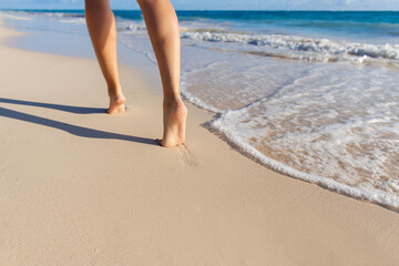 Low angle view of women's legs walking away along white sandy beach at the edge of the ocean water with gentle surf, copy space
