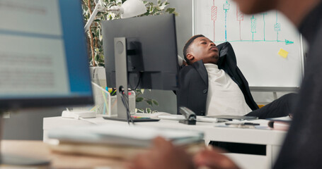 Dark-skinned boss sits on chair with feet on desk, holding tablet in hands, surfing the Internet,...