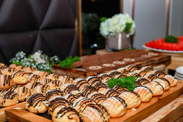 A party table features various sweet treats, including cream puffs with chocolate and cream toppings, chocolate cookies, and a fruit plate. The arrangement is enticing and beautifully presented