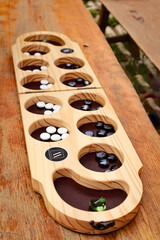 A wooden Mancala board features black and white stones arranged neatly in its pits, set on a wooden table. The "MOMOWOOD" logo adds elegance to the simple yet strategic board game