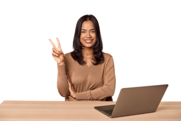 Filipino woman at desk with laptop showing number two with fingers.