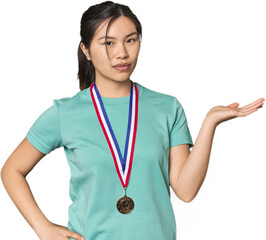 Chinese athlete showing a medal showing a copy space on a palm and holding another hand on waist.