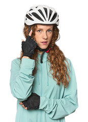 Young redhead cycling in studio pointing temple with finger, thinking, focused on a task.