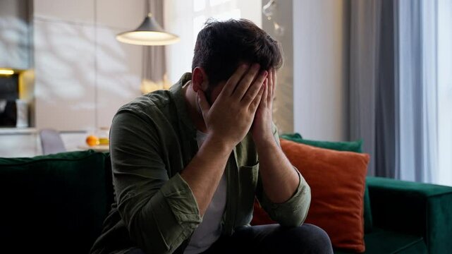 Stressed sick unhappy Caucasian man business male businessman guy homeowner unwell troubled buyer client customer sitting couch covering face with hands stress gesture problems headache pain at home
