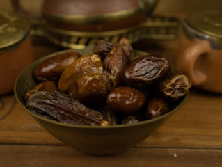 Dates in brass bowl wooden surface no people warm lighting traditional Middle Eastern setting