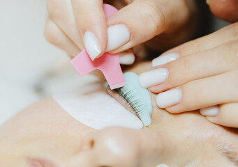 Girl cosmetologist laminates and paints woman eyelashes