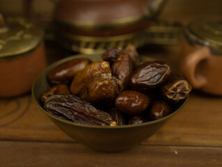 Dates in brass bowl wooden surface no people warm lighting traditional Middle Eastern setting