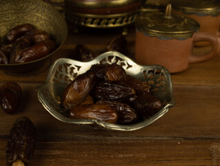 Dates in brass bowl wooden surface no people warm lighting traditional Middle Eastern setting