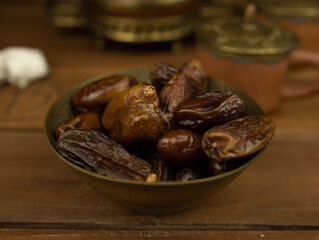 Dates in brass bowl wooden surface no people warm lighting traditional Middle Eastern setting