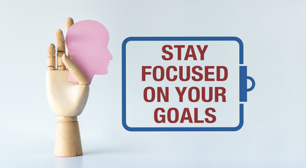 A hand holding a pink head with the words Stay focused on your goals