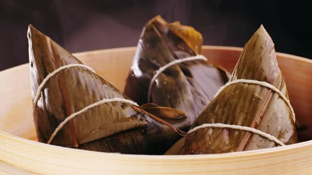 Hand holding zongzi (rice dumpling) with savoury fillings wrapped in bamboo or reed leaves.