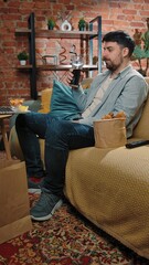 Man spending time at home with fast food delivery, sits on couch watching tv, eating dipping fried chicken in sauce, drinking cola, enjoying the taste.