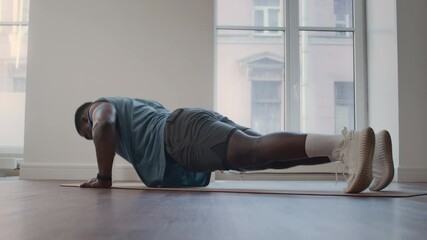 Strong African American man performing push-ups on mat during full body workout in home gym - Powered by Adobe
