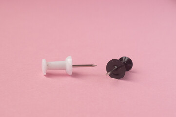 Black and white push pins on pink paper background close-up