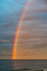 A shining rainbow in the gloomy sky over the sea. Low clouds over the water in the bay.