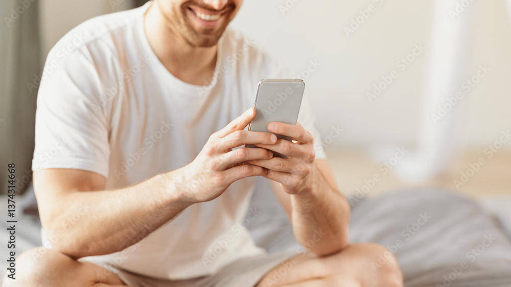 Poster unrecognizable guy using mobile phone with great mobile application sitting on bed in bedroom at hom