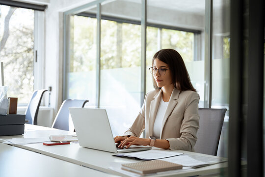 Concentrated latin hispanic woman using computer technology for work online. Young professional it specialist latin hispanic business lady working on laptop pc sitting at desk in modern office. Wide