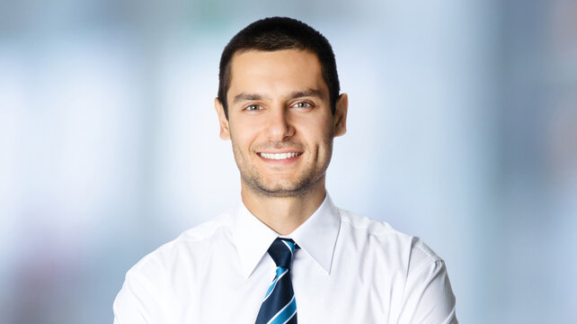 Portrait image - happy smile brunette business man in white corporate shirt, blue tie, stand against blurred office background. Businessman, bank account manager, lawyer, teacher, student, sales agent