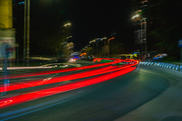 Red neon trails in night on city road long exposure. Multiple red light trails curve along city...
