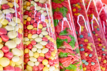 Brightly colored bags filled with a variety of candies line the shelves in a market. The vibrant colors attract attention while sweet scents fill the air, enticing shoppers